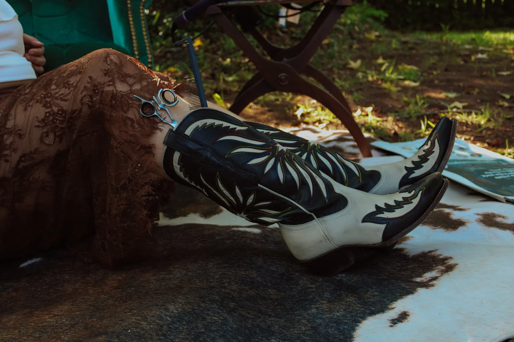 Embroidered western boots crossed on a cowhide rug beside shears and a comb