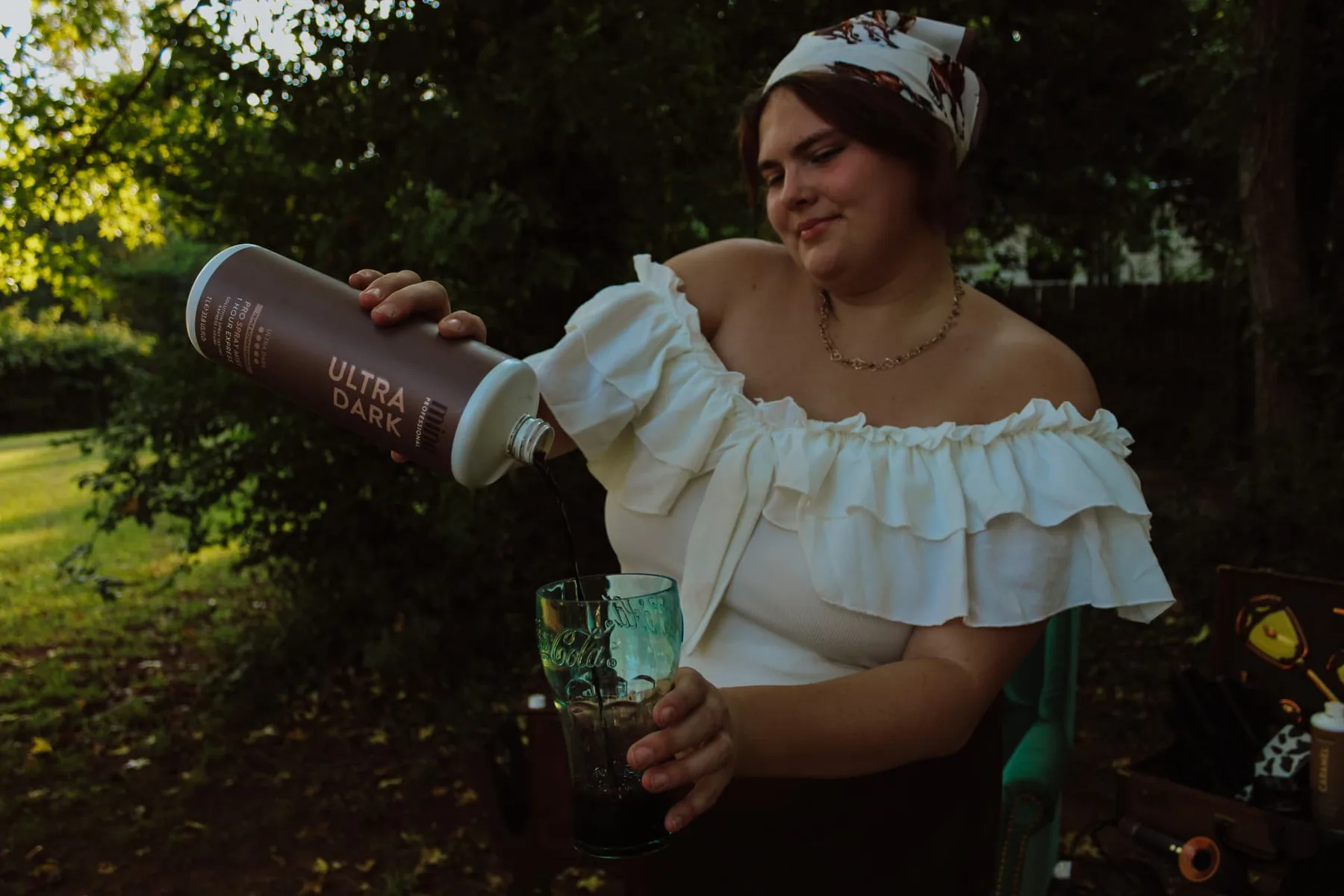 Maddie in a horse-print scarf pouring a spray tan solution into a glass outdoors
